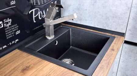 Modern design chrome water tap over black stone kitchen sink on table top made of wood with chalk lettering background